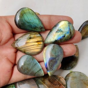 May include: A collection of teardrop-shaped labradorite gemstone cabochons in various shades of green, blue, and gold. The stones have a iridescent sheen and are perfect for jewelry making.