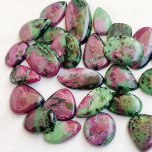 May include: A collection of 18 green and pink gemstone cabochons, with black and gold inclusions. The stones are all pear-shaped and have a smooth, polished finish.