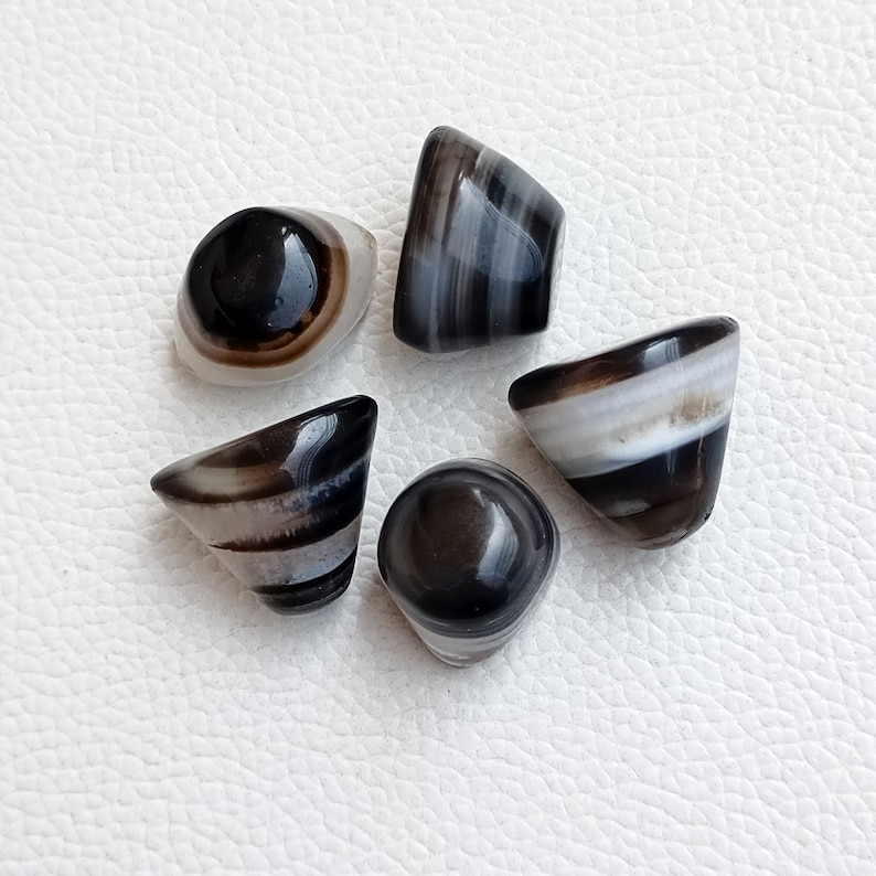 May include: Five black and white agate cabochons with a conical shape. The cabochons have a banded pattern of black, white, and brown.