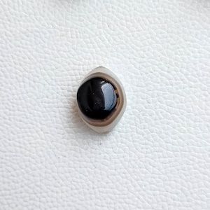 May include: A black and white agate stone with a round, black center. The stone is polished and has a smooth surface.
