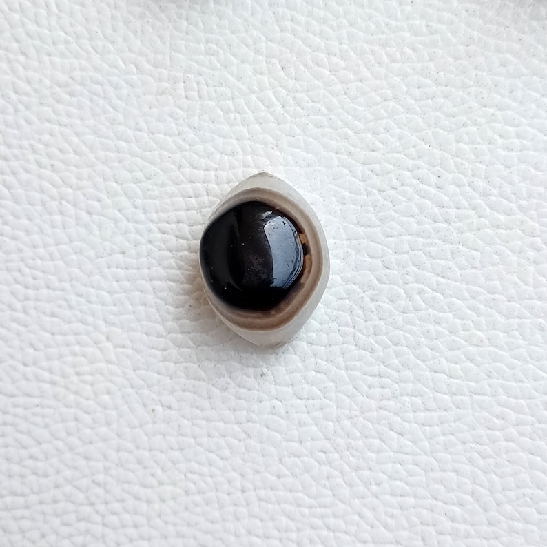 May include: A black and white agate stone with a round, black center. The stone is polished and has a smooth surface.