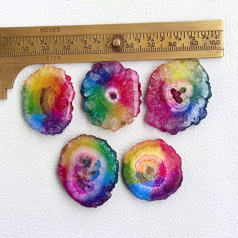 May include: Five rainbow agate slices, each with a different color pattern and a white center. The agate slices are approximately 1 inch in diameter.