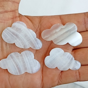 Pode incluir: Quatro nuvens de cristal de selenite branca com um padrão estriado. As nuvens são esculpidas em selenite natural e têm um acabamento liso e polido.