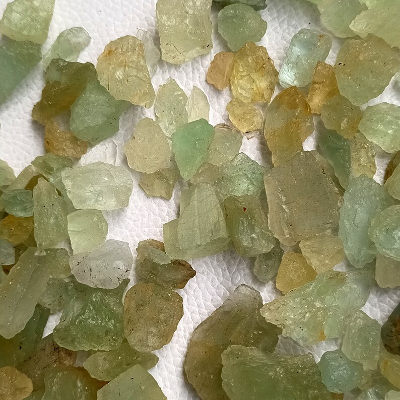 May include: A collection of rough, green and yellow gemstones. The stones are various sizes and shapes, and have a translucent appearance.