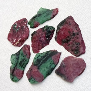 May include: A collection of seven rough, uncut ruby zoisite gemstones. The stones are a mix of pink, green, and black.