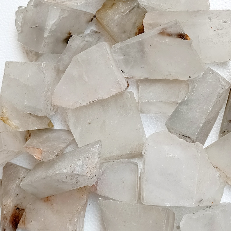 May include: A collection of raw, clear quartz crystal chunks. The crystals vary in size and shape, with a translucent appearance and subtle variations in color, ranging from clear to milky white. Some pieces have small, natural inclusions.