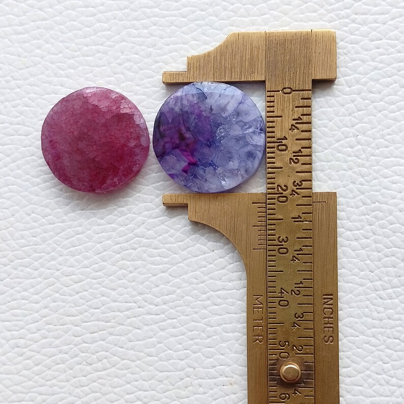 May include: Two round agate slices, one purple and one pink, are measured with a ruler. The purple agate slice measures 1 1/4 inches in diameter.