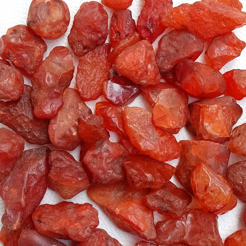 Op de afbeelding: Een verzameling carneol edelstenen, elk met een unieke vorm en grootte. De carneol stenen zijn diep rood-oranje van kleur en hebben een gladde, gepolijste afwerking.