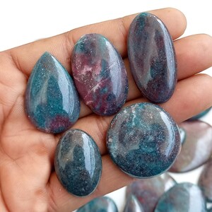 May include: A collection of polished green and pink gemstone cabochons, with a variety of shapes and sizes. The stones have a mottled appearance, with swirls of color throughout.