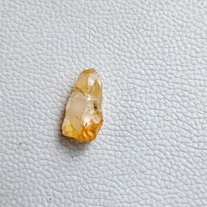 May include: A small, translucent, yellow-orange crystal with a pointed tip. The crystal has a rough, natural texture.