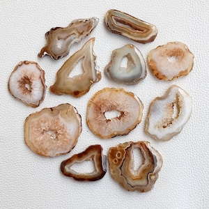 May include: Assortment of 10 agate slices with natural brown and white patterns. Each slice has a unique shape and size, with some featuring a hole in the centre.