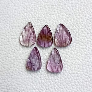 May include: Six purple and clear carved gemstone pendants in a teardrop shape. The pendants have a leaf design carved into them.