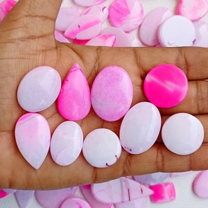 Könnte beinhalten: Eine Sammlung von rosa und weißen Achat-Cabochons, einige in Tropfenform, andere rund und einige oval. Die Cabochons sind glatt und poliert, mit einer Vielzahl von Mustern und Wirbeln.