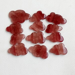 Pode incluir: Treze cabochões de pedra preciosa em forma de nuvem de cor vermelha. Os cabochões são translúcidos e têm um padrão estriado.
