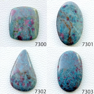 May include: Four polished gemstones in various shapes: a square, an oval, a teardrop, and a rounded oval. Each stone has a blue-green base color with red and maroon inclusions. The stones are numbered 7300, 7301, 7302, and 7303.