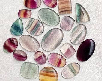 May include: Assortment of 19 fluorite cabochons in various colors and patterns, including green, purple, pink, and white. The cabochons are smooth and polished, with a variety of shapes and sizes.