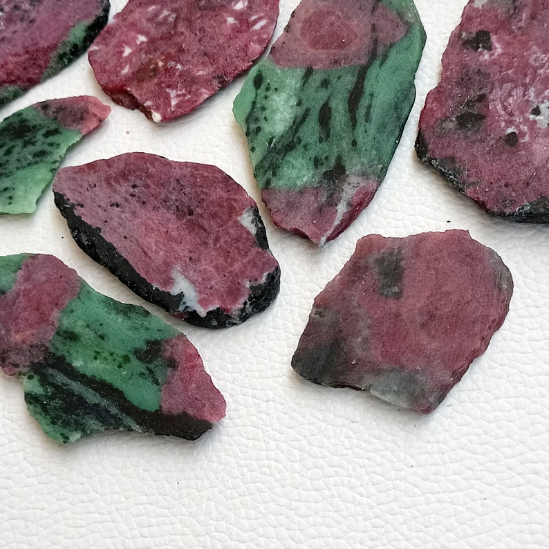 Może przedstawiać: Zbi&oacute;r zielonych i r&oacute;żowych odłamk&oacute;w kamieni szlachetnych. Odłamki mają nieregularny kształt i szorstką, naturalną fakturę.