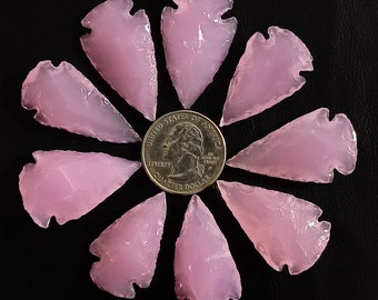 Puede incluir: Diez puntas de flecha rosas dispuestas en círculo alrededor de una moneda de un cuarto de dólar estadounidense. Las puntas de flecha están hechas de un material translúcido y tienen un acabado liso y pulido.
