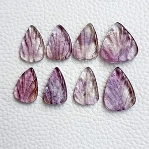 May include: Eight purple and clear carved gemstone triangle pendants. The pendants have a fan-shaped design and are approximately 2.5 cm in length.
