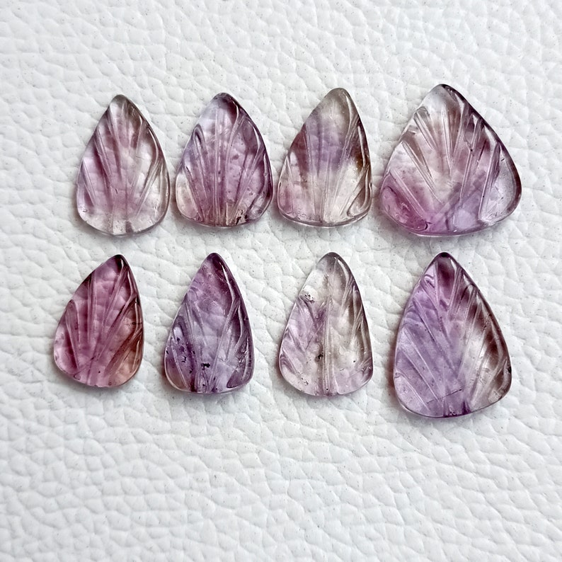 May include: Eight purple and clear carved gemstone triangle pendants. The pendants have a fan-shaped design and are approximately 2.5 cm in length.