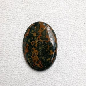 May include: Oval shaped green, brown, and white ocean jasper cabochon with a polished finish.