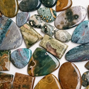 May include: A collection of polished green, blue, brown, and gray stones with various patterns. The stones are irregularly shaped and have a smooth, polished finish.