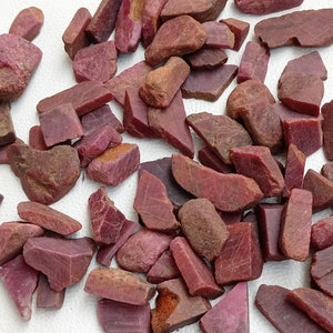 May include: A collection of rough, red ruby gemstones. The ruby pieces are various shapes and sizes, with some having a more polished look.