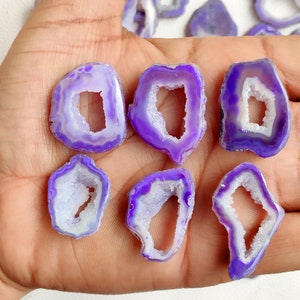May include: Several polished agate slices in shades of purple and white. Each slice has a unique shape and a hollow, crystal-filled centre. The outer edges are a vibrant purple, transitioning to a lighter hue towards the inner core, creating a natural geode effect.