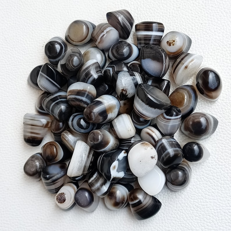 May include: A collection of black and white banded agate stones. The stones are smooth and polished, and they have a variety of shapes and sizes.