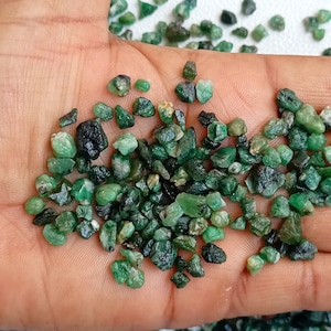 May include: A close-up of a handful of small, rough, green emerald gemstones.