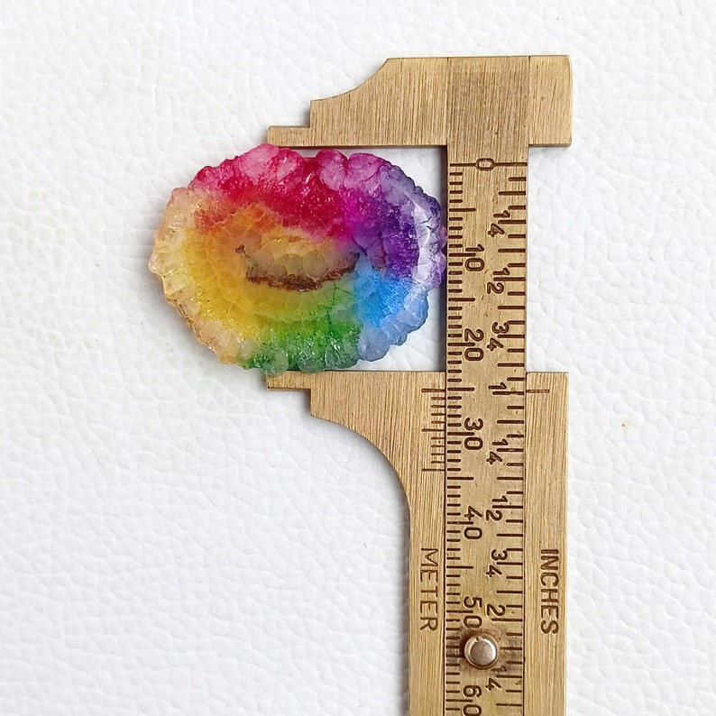 May include: A rainbow agate geode slice measuring approximately 1 1/4 inches in diameter. The geode has a natural, irregular shape and features a variety of colors, including red, orange, yellow, green, blue, and purple.