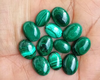 Puede incluir: Una colección de piedras preciosas de malaquita de forma ovalada en varios tonos de verde. Las piedras son lisas y pulidas, con intrincados patrones y remolinos.