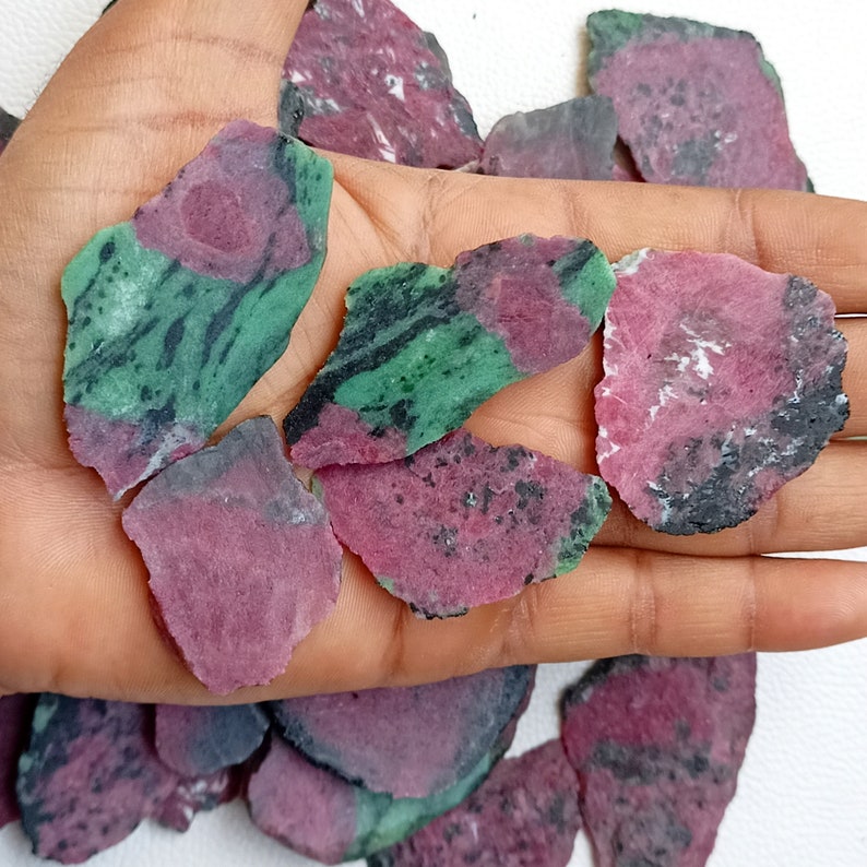 Może przedstawiać: Kolekcja surowych, zielonych i r&oacute;żowych odłamk&oacute;w kamieni szlachetnych. Odłamki mają nieregularny kształt i marmurkowy wygląd.