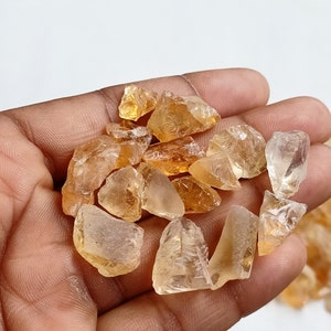 May include: A collection of raw, natural citrine crystals in various sizes and shapes. The crystals are a light to medium amber color and have a translucent to transparent appearance.