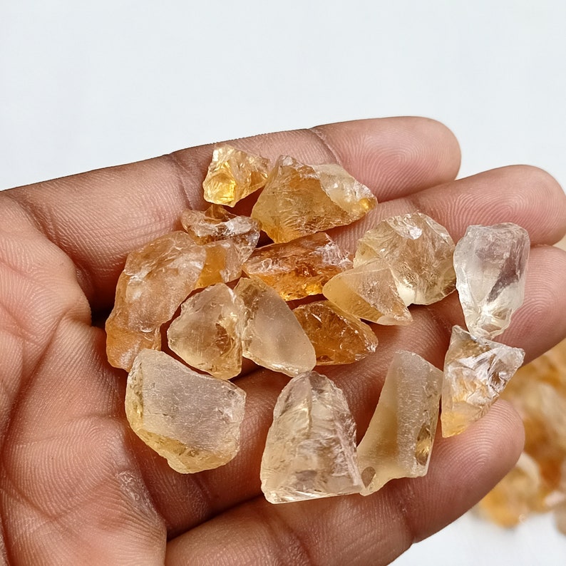 May include: A collection of raw, natural citrine crystals in various sizes and shapes. The crystals are a light to medium amber color and have a translucent to transparent appearance.