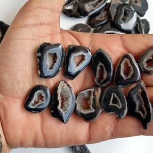 Puede incluir: Una colección de rodajas de ágata negra con formaciones cristalinas naturales y centros abiertos. Las rodajas de ágata tienen una forma irregular y una superficie lisa y pulida.