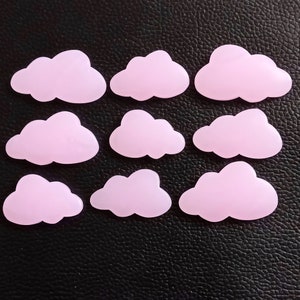 Könnte beinhalten: Zehn rosa wolkenförmige Leucht-Sticker. Die Sticker sind in drei Reihen auf einer schwarzen, strukturierten Oberfläche angeordnet.
