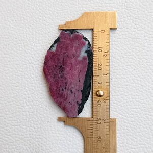 Może przedstawiać: Surowy, r&oacute;żowo-czarny kamień szlachetny o długości około 3,5 cm. Kamień szlachetny jest mierzony linijką.