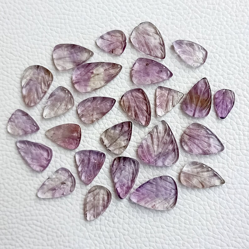 May include: A collection of 25 purple and clear faceted gemstone pendants with a leaf design. The pendants are carved from amethyst and are ideal for jewellery making.