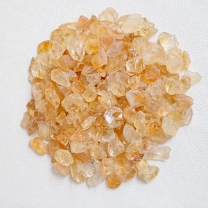 May include: A pile of small, translucent, yellow-orange citrine crystals. The crystals are irregularly shaped and have a natural, rough texture.