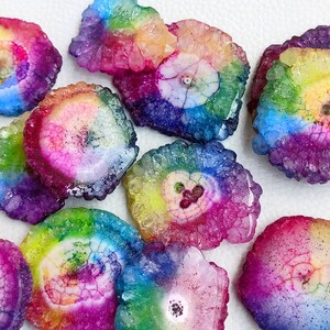 May include: A collection of rainbow agate slices with a variety of colors and patterns. The slices are all different sizes and shapes, and they have a natural, rough texture.
