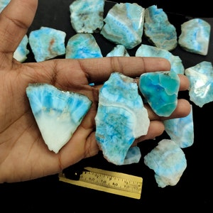 Könnte beinhalten: Eine Sammlung von blau-weißen Ozeanjaspis-Steinen, auch bekannt als blauer Calcit, in verschiedenen Formen und Größen. Die Steine sind auf einer Hand angeordnet, mit einem Lineal im Hintergrund.
