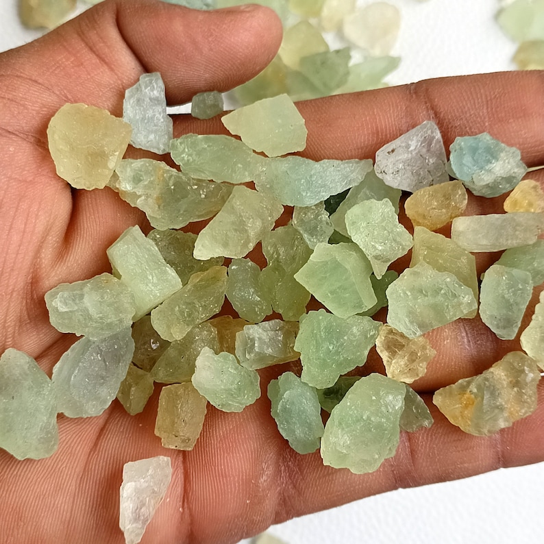 May include: A collection of small, rough, green and yellow aquamarine crystals. The crystals are various shapes and sizes, and have a translucent appearance.
