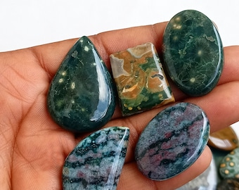 May include: Assortment of green, brown, and purple ocean jasper cabochons with white and gold flecks. The cabochons are various shapes and sizes, including oval, teardrop, and square.