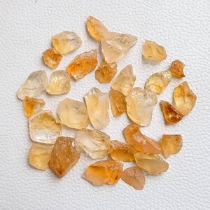 May include: A collection of raw, natural citrine crystals in various sizes and shapes. The crystals are a light to medium yellow color and have a translucent appearance.