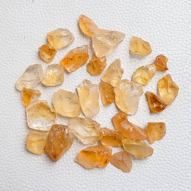 May include: A collection of raw, natural citrine crystals in various sizes and shapes. The crystals are a light to medium yellow color and have a translucent appearance.
