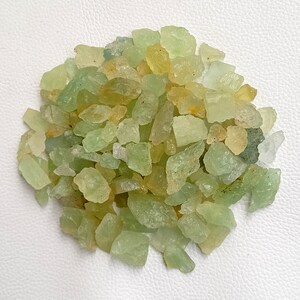 May include: A pile of green and yellow aquamarine rough gemstones. The stones are irregular in shape and size, and have a translucent appearance.