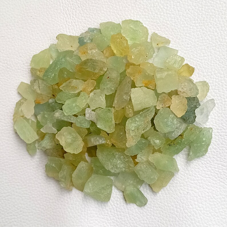 May include: A pile of green and yellow aquamarine rough gemstones. The stones are irregular in shape and size, and have a translucent appearance.