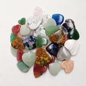 May include: A collection of heart-shaped gemstone cabochons in various colors, including green, blue, red, brown, white, and pink. The stones are polished and have a smooth, glossy finish.