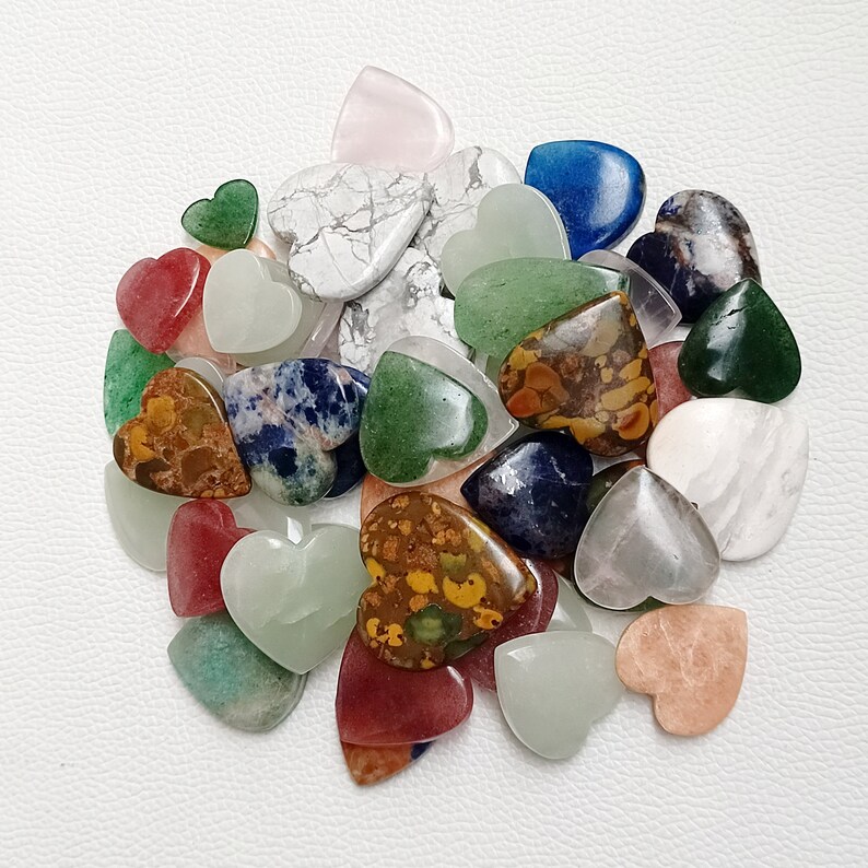 May include: A collection of heart-shaped gemstone cabochons in various colors, including green, blue, red, brown, white, and pink. The stones are polished and have a smooth, glossy finish.